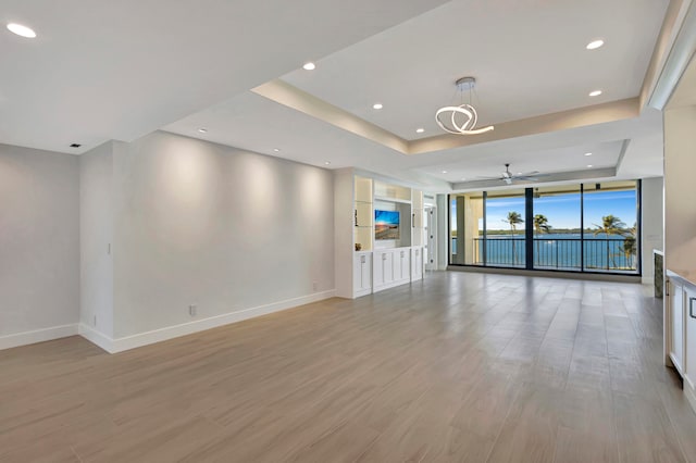 unfurnished living room with ceiling fan, light hardwood / wood-style floors, and a raised ceiling