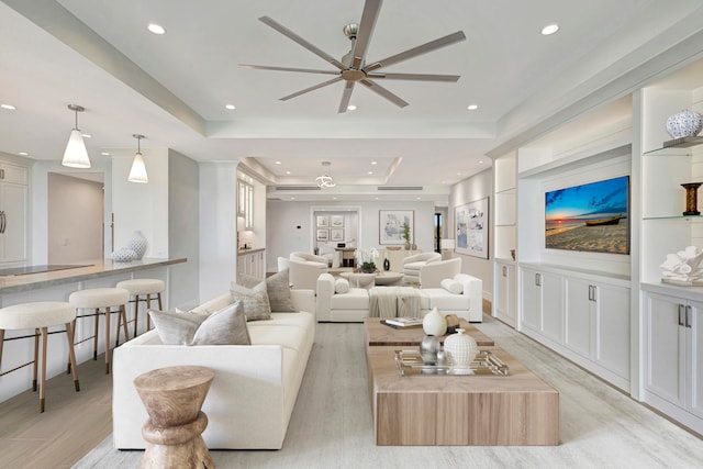 living room with ceiling fan, a raised ceiling, light hardwood / wood-style floors, and built in features