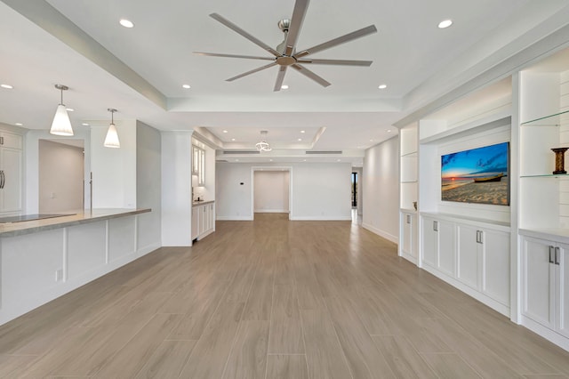 unfurnished living room with ceiling fan, light hardwood / wood-style flooring, and a tray ceiling