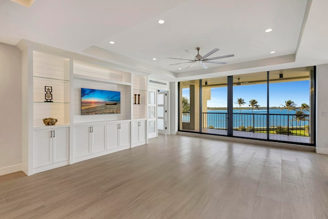 unfurnished living room featuring ceiling fan, built in features, floor to ceiling windows, a tray ceiling, and light hardwood / wood-style floors