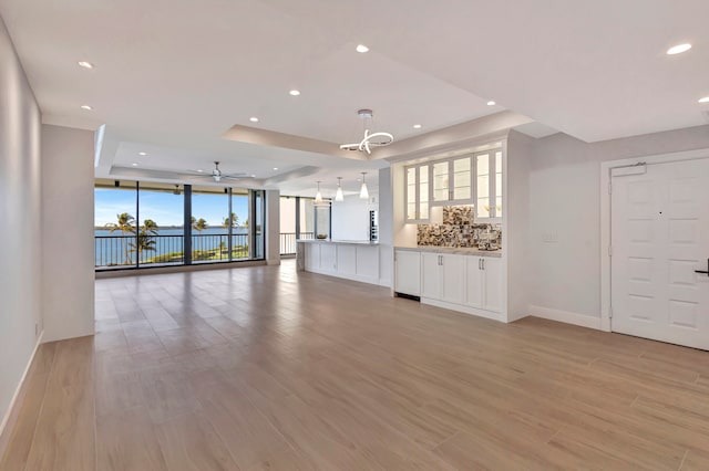 unfurnished living room featuring ceiling fan, light wood-type flooring, and a raised ceiling