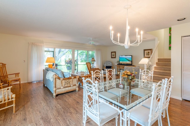 dining space with stairs, ceiling fan with notable chandelier, baseboards, and wood finished floors