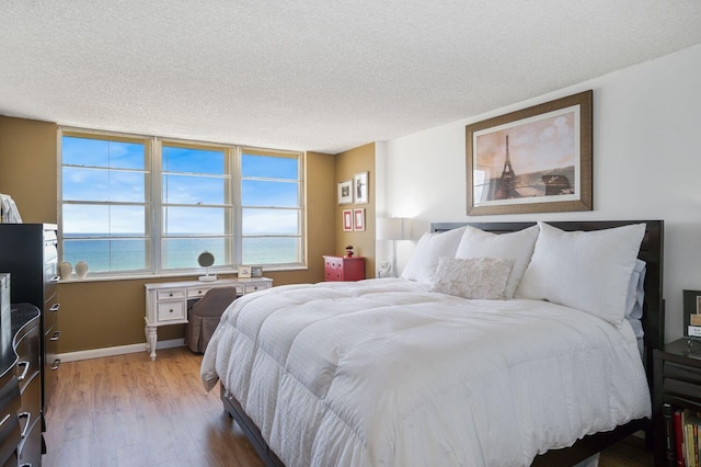 bedroom with a textured ceiling, light hardwood / wood-style flooring, and a water view