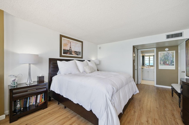 bedroom with light hardwood / wood-style flooring, a textured ceiling, and ensuite bath