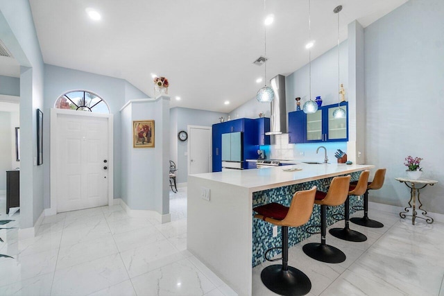 kitchen featuring wall chimney exhaust hood, a kitchen breakfast bar, light tile patterned floors, kitchen peninsula, and blue cabinets