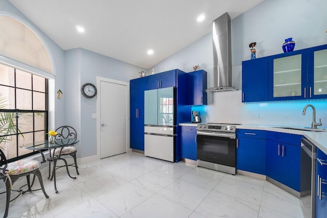 kitchen with appliances with stainless steel finishes, sink, blue cabinetry, and wall chimney range hood