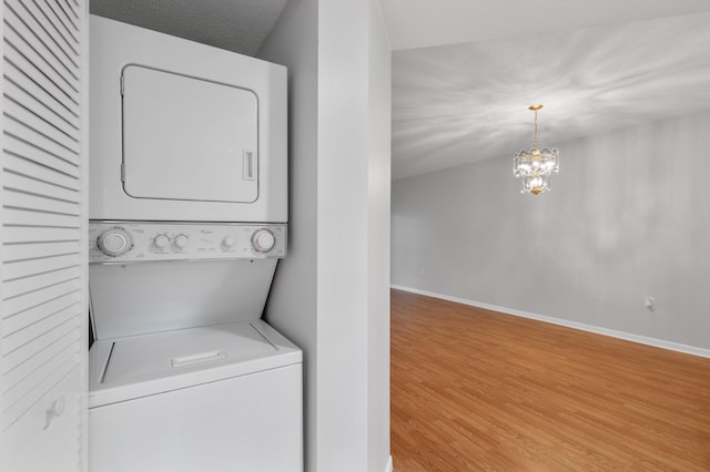 laundry area with light hardwood / wood-style flooring, a textured ceiling, an inviting chandelier, and stacked washer and clothes dryer