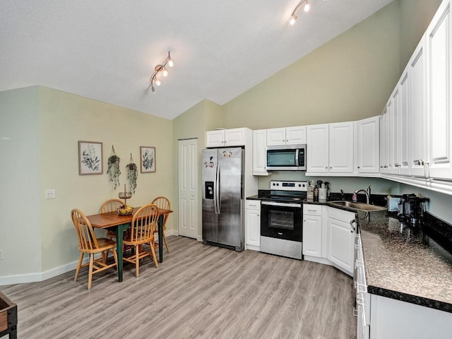 kitchen with high vaulted ceiling, white cabinets, sink, light hardwood / wood-style floors, and stainless steel appliances