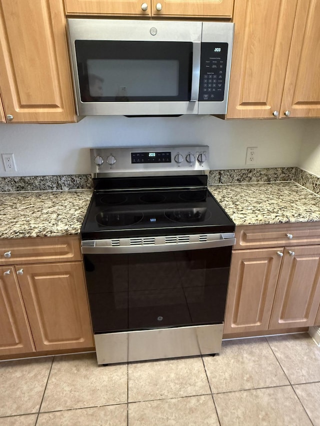 kitchen featuring light tile patterned flooring, appliances with stainless steel finishes, and light stone countertops