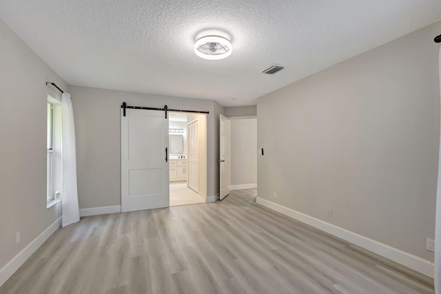 unfurnished bedroom featuring connected bathroom, light hardwood / wood-style flooring, a textured ceiling, and a barn door