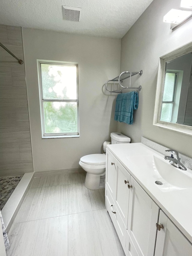 bathroom featuring vanity, toilet, tiled shower, and a textured ceiling