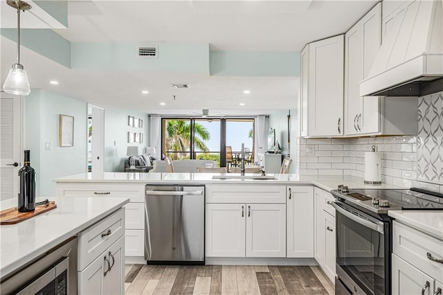 kitchen featuring custom range hood, appliances with stainless steel finishes, light hardwood / wood-style floors, and white cabinetry