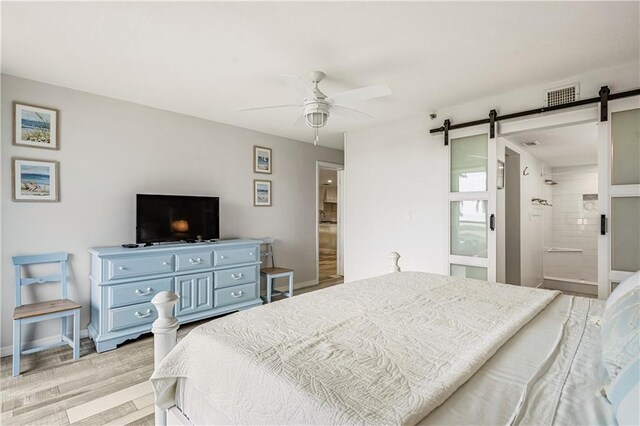 bedroom with ceiling fan, connected bathroom, light hardwood / wood-style floors, and a barn door