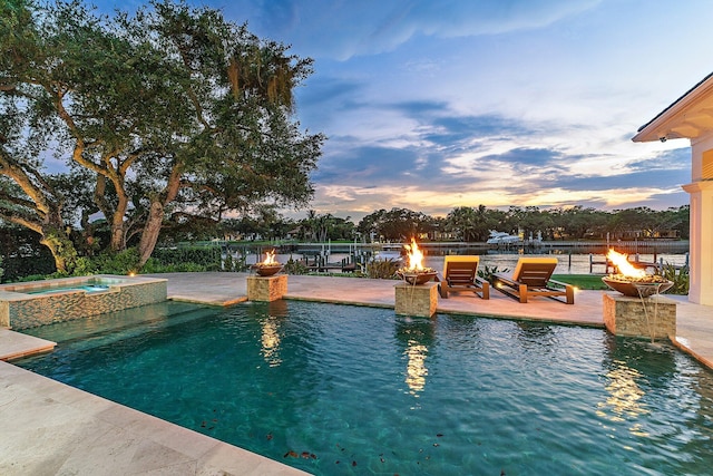 pool at dusk featuring an in ground hot tub, a patio area, and a fire pit