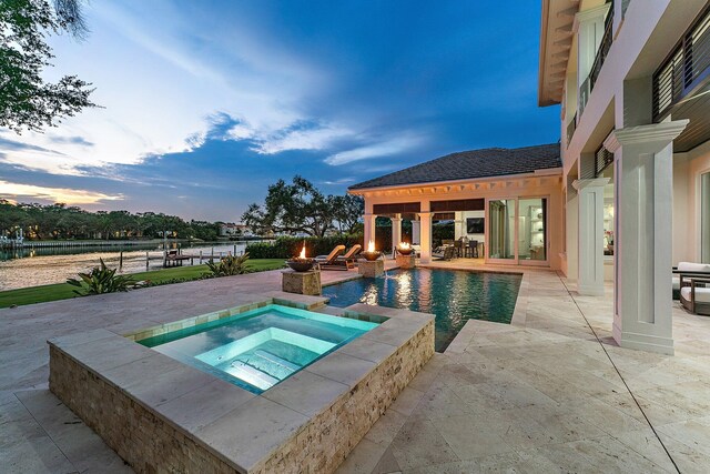 pool at dusk featuring an in ground hot tub and a patio