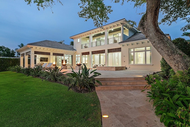 back house at dusk with a patio, a gazebo, a lawn, and a balcony