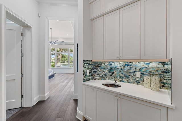 bar featuring sink, ornamental molding, white cabinets, dark wood-type flooring, and decorative backsplash