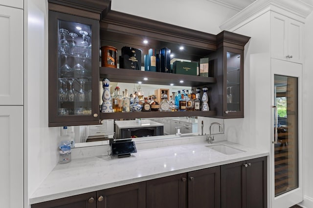 bar featuring wine cooler, sink, light stone countertops, and dark brown cabinets