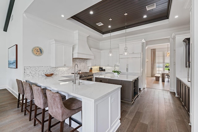 kitchen featuring dark hardwood / wood-style floors, kitchen peninsula, decorative light fixtures, a raised ceiling, and white cabinets