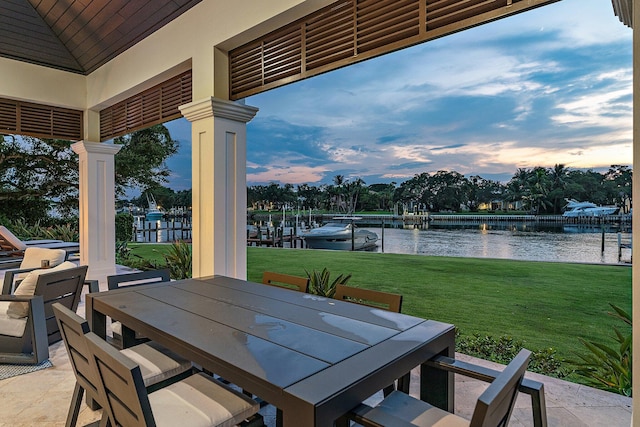 patio terrace at dusk with a water view, a lawn, and a dock