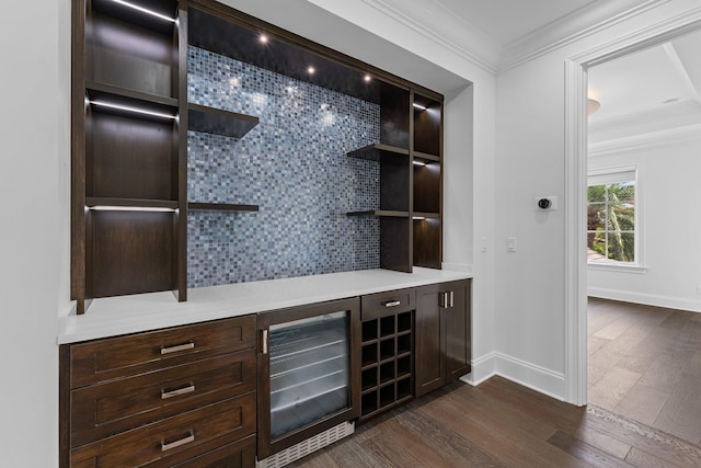 bar with ornamental molding, dark brown cabinetry, tasteful backsplash, beverage cooler, and dark hardwood / wood-style flooring