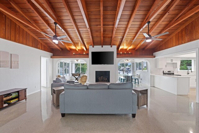 living room with wood ceiling, ceiling fan, beamed ceiling, and a brick fireplace