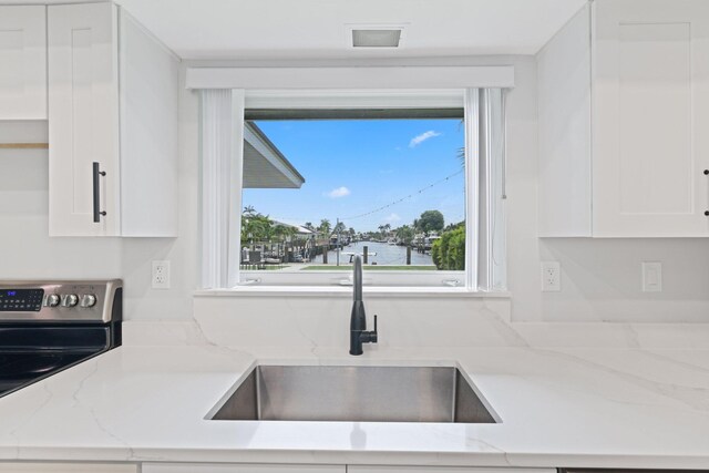 kitchen featuring sink, stainless steel electric range, light stone countertops, and white cabinets