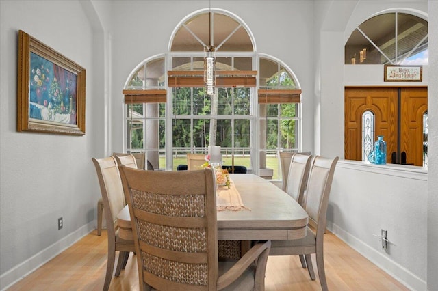 dining space featuring light wood-type flooring and a towering ceiling