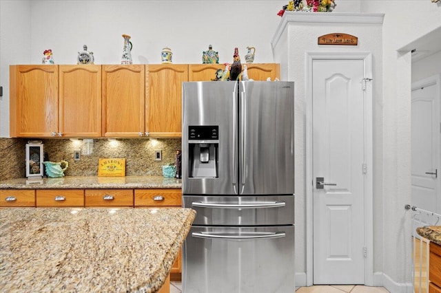 kitchen with decorative backsplash, light tile patterned flooring, stainless steel fridge with ice dispenser, and light stone counters