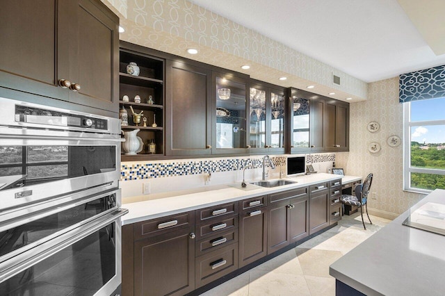 kitchen featuring light tile patterned floors, backsplash, dark brown cabinetry, and stainless steel double oven