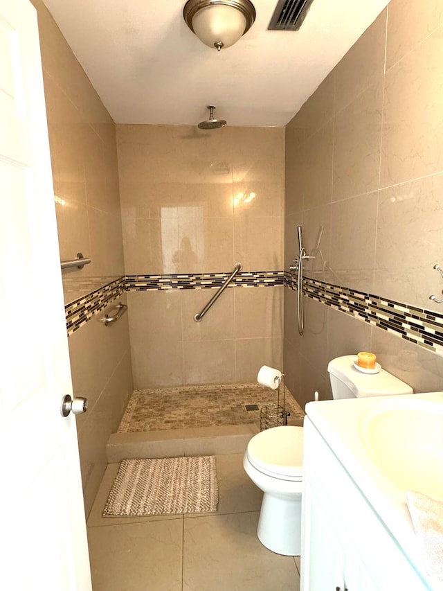 bathroom featuring vanity, tile patterned floors, toilet, tile walls, and a tile shower