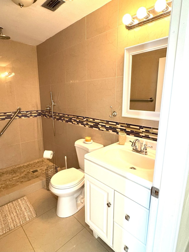 bathroom featuring vanity, a shower, tile patterned floors, toilet, and tile walls