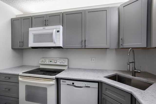 kitchen featuring white appliances, light stone countertops, gray cabinets, and a sink