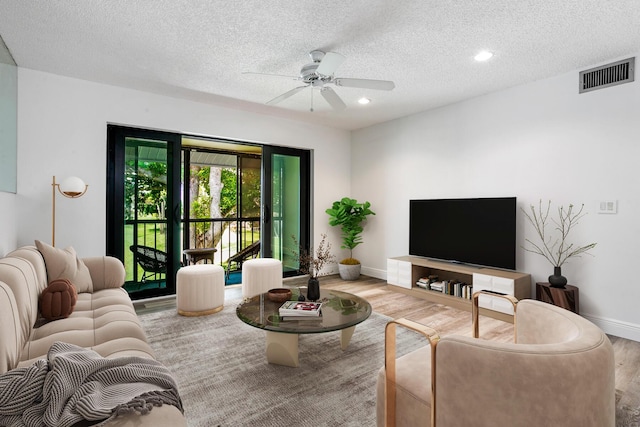 living room featuring a ceiling fan, baseboards, wood finished floors, visible vents, and a textured ceiling