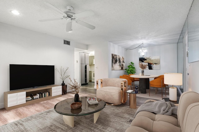 living area with visible vents, a textured ceiling, wood finished floors, and ceiling fan with notable chandelier