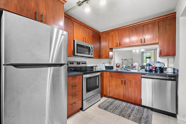 kitchen with a textured ceiling, light tile patterned floors, appliances with stainless steel finishes, sink, and rail lighting