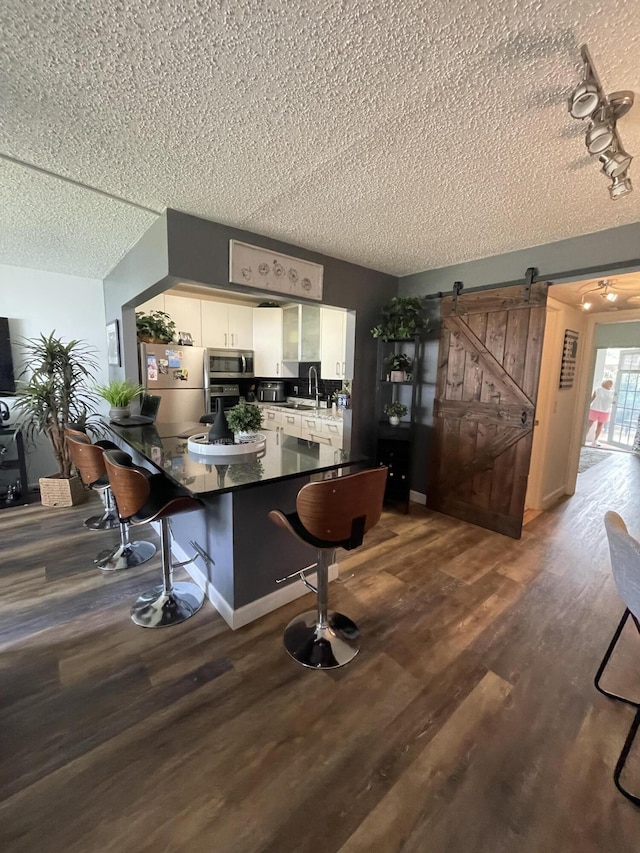 kitchen featuring a textured ceiling, appliances with stainless steel finishes, white cabinetry, a barn door, and hardwood / wood-style floors