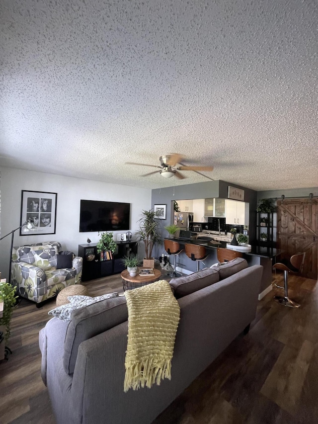 living room with hardwood / wood-style floors, a barn door, a textured ceiling, and ceiling fan