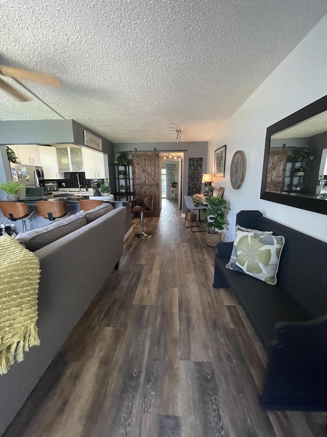 living room featuring ceiling fan, a textured ceiling, a barn door, and hardwood / wood-style floors