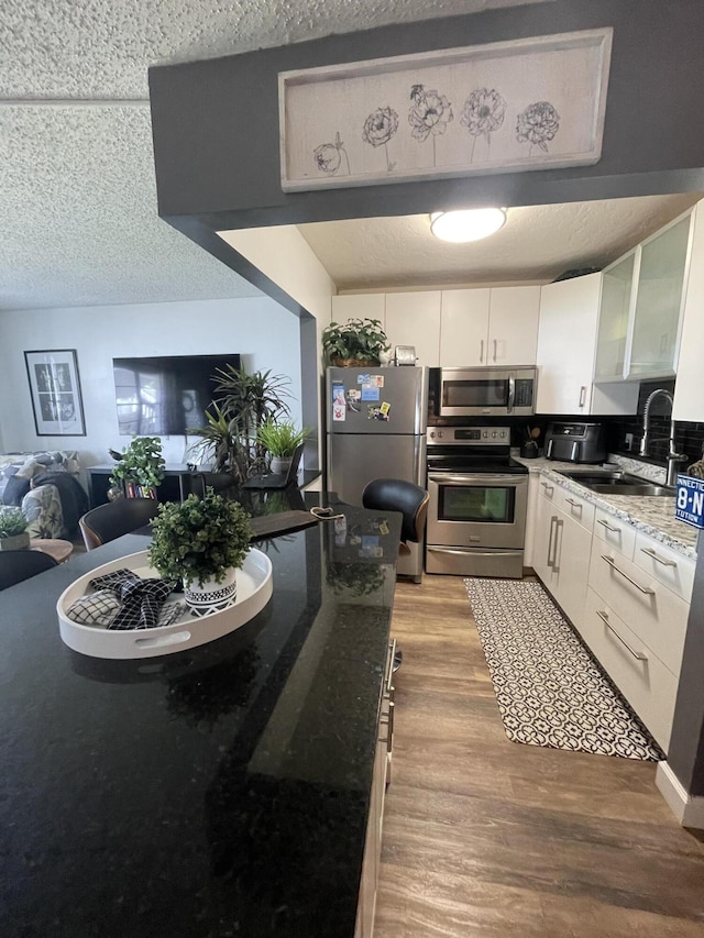 kitchen with light hardwood / wood-style flooring, appliances with stainless steel finishes, sink, and dark stone counters