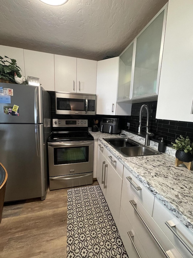 kitchen with decorative backsplash, light hardwood / wood-style flooring, white cabinetry, appliances with stainless steel finishes, and sink