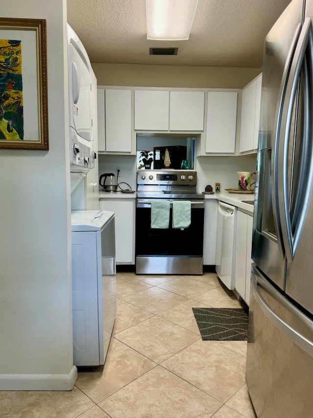 kitchen featuring light tile patterned flooring, stacked washing maching and dryer, stainless steel appliances, and white cabinets