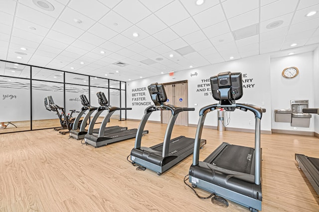 exercise room featuring a paneled ceiling and light wood-type flooring