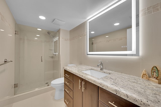 bathroom featuring tile walls, toilet, vanity, tile patterned flooring, and a shower with shower door