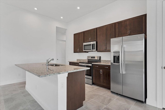 kitchen with light stone countertops, dark brown cabinets, stainless steel appliances, sink, and a center island with sink