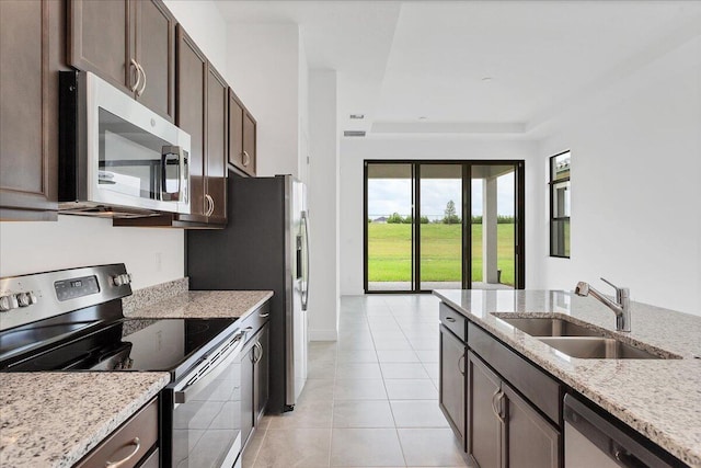 kitchen with light stone countertops, appliances with stainless steel finishes, dark brown cabinetry, and sink