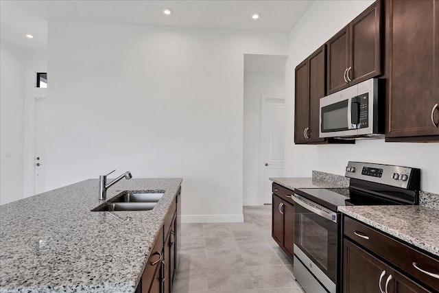 kitchen with sink, stainless steel appliances, light stone counters, dark brown cabinets, and light tile patterned floors