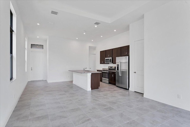 kitchen with appliances with stainless steel finishes, dark brown cabinets, sink, light tile patterned floors, and an island with sink