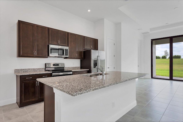 kitchen with a center island with sink, sink, light stone countertops, and stainless steel appliances