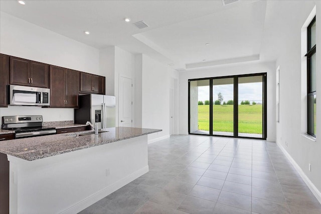 kitchen with appliances with stainless steel finishes, light stone counters, dark brown cabinets, a kitchen island with sink, and sink